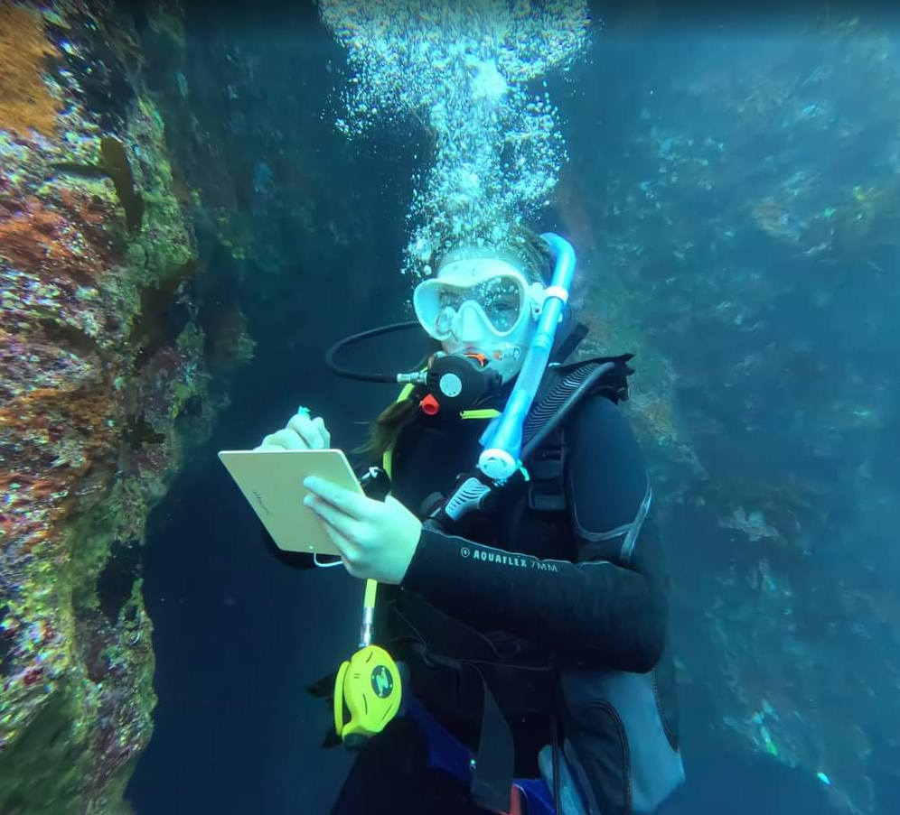Kyra Barker scuba diving underwater while writing on a slate